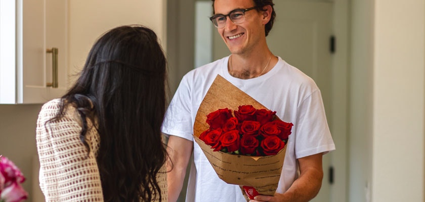 A smiling man presents a bouquet of red roses to a woman, capturing a heartfelt moment.