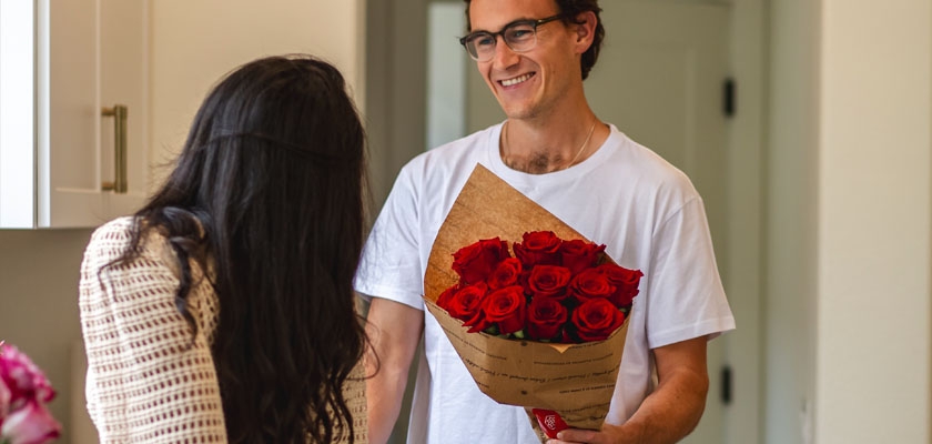 A smiling man presents a bouquet of red roses to a woman, capturing a heartfelt moment.