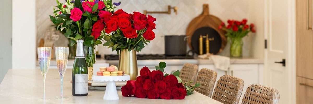Elegant kitchen setting featuring vibrant red roses, champagne, and sweet treats.