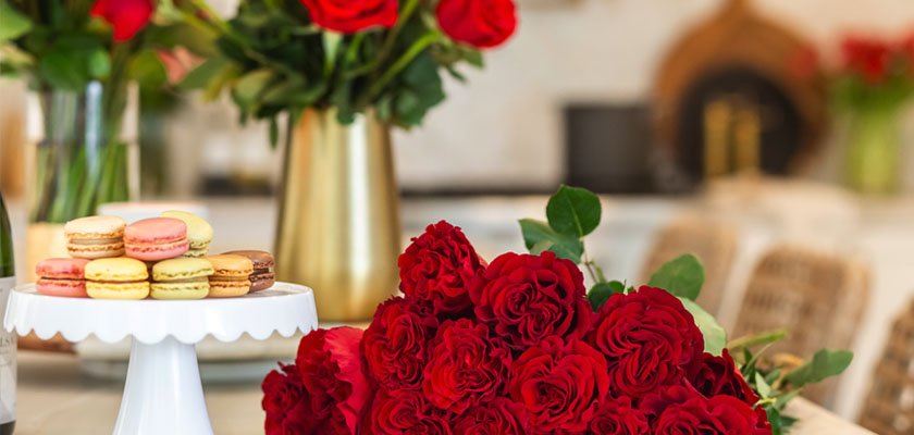Vibrant red rose bouquet elegantly displayed with colorful macarons in a stylish kitchen setting.