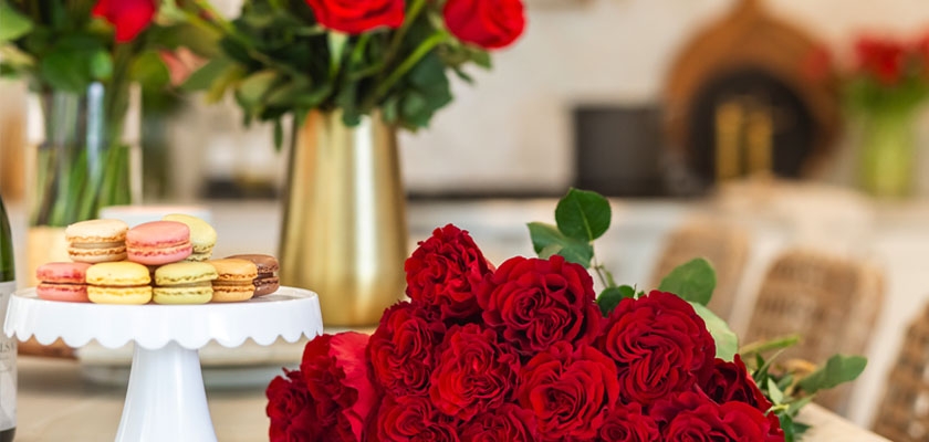 Vibrant red rose bouquet elegantly displayed with colorful macarons in a stylish kitchen setting.