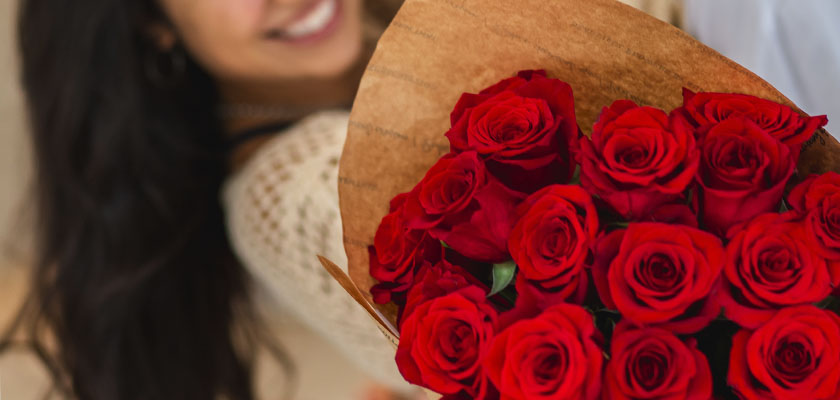 A cheerful woman holding a stunning bouquet of vibrant red roses wrapped in brown paper.