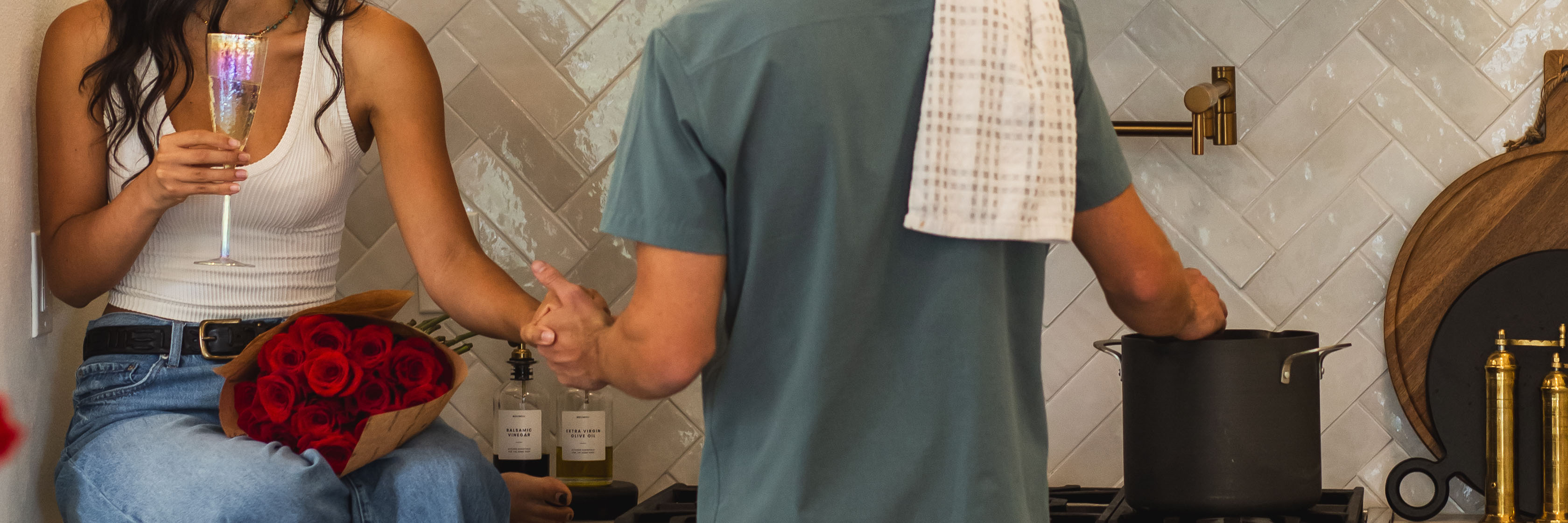 A couple celebrates together in a cozy kitchen, surrounded by roses and champagne.