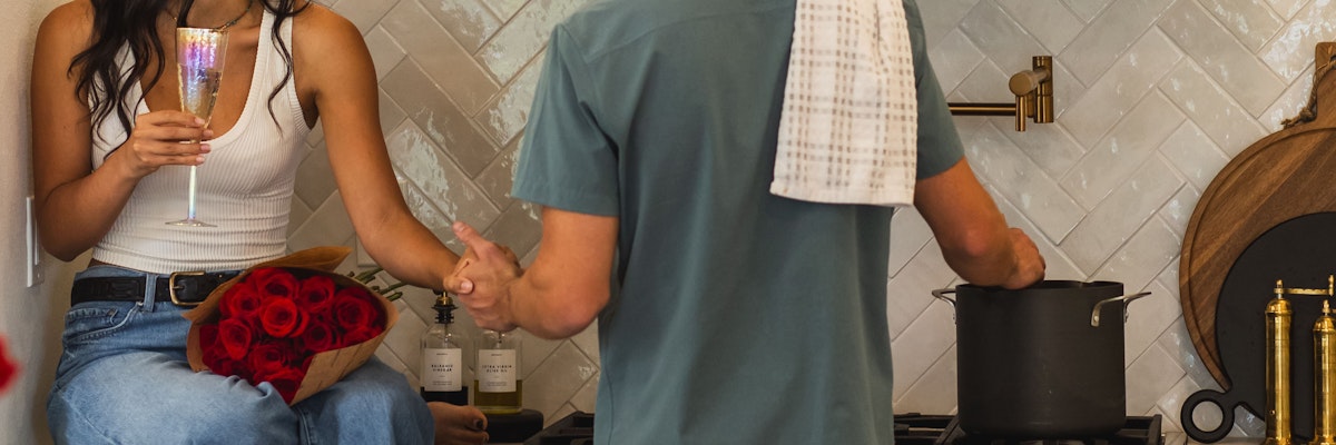 A couple celebrates together in a cozy kitchen, surrounded by roses and champagne.
