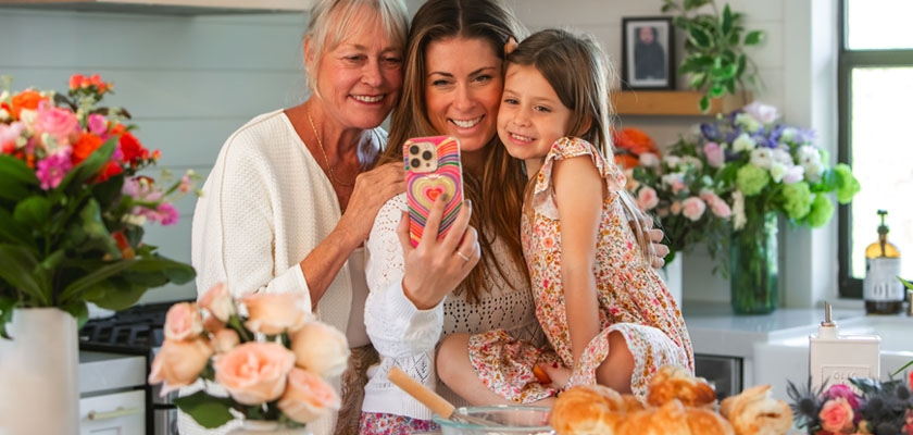 A joyful family moment as three generations capture a selfie in a blooming kitchen.