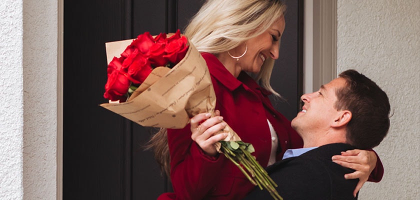 A joyful couple at the doorstep, celebrating love with a bouquet of vibrant red roses.