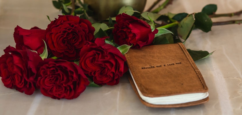 A lovely arrangement of red roses beside a charming leather notebook inviting romance.