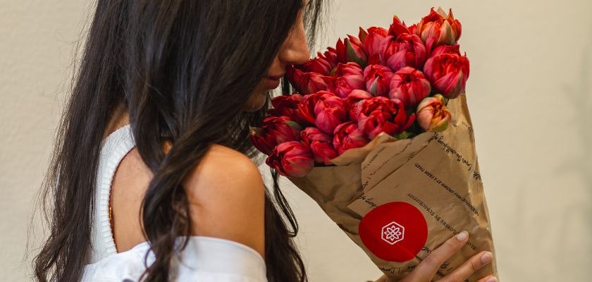 A woman smelling a vibrant bouquet of red tulips, beautifully wrapped for gifting.