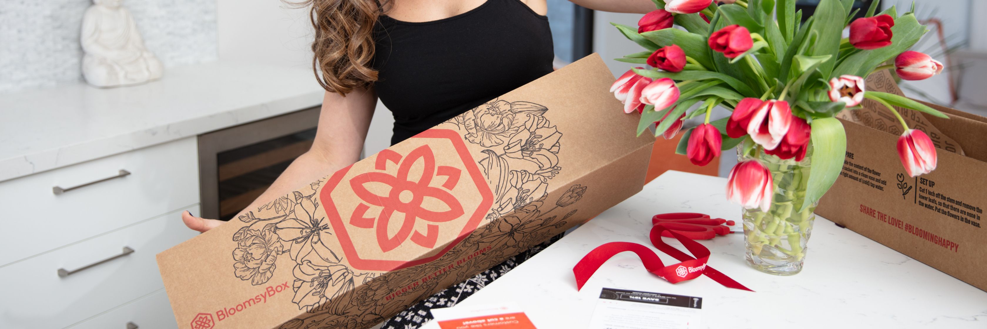 A woman unboxing a vibrant tulip bouquet from BloomsyBox, featuring fresh red blooms.