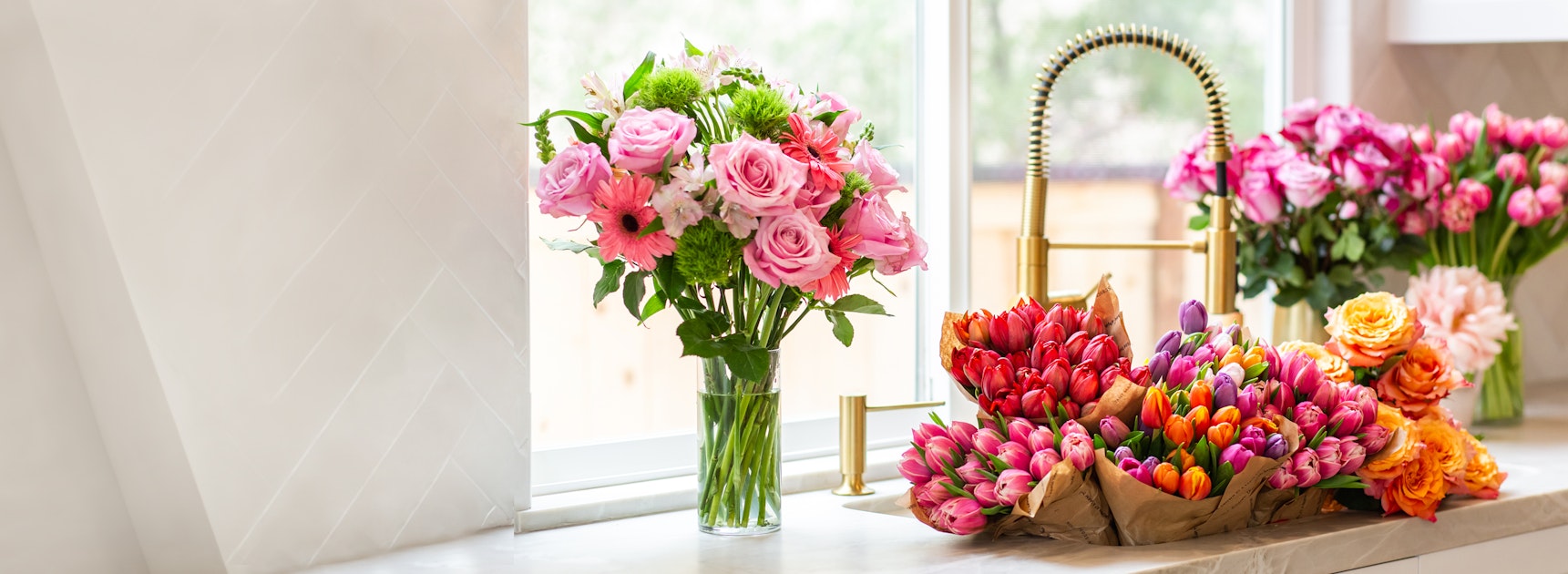 A vibrant floral display featuring pink roses and colorful tulips in a bright kitchen setting.