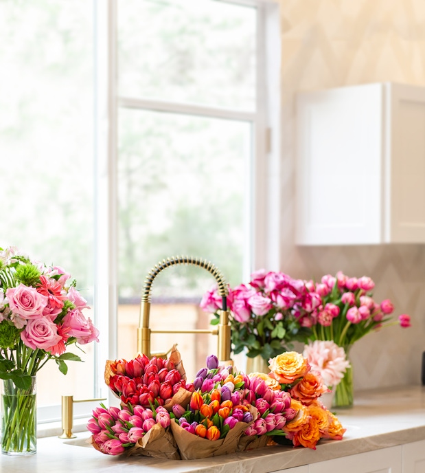 Vibrant floral display featuring tulips, roses, and peonies in a sunny kitchen setting.