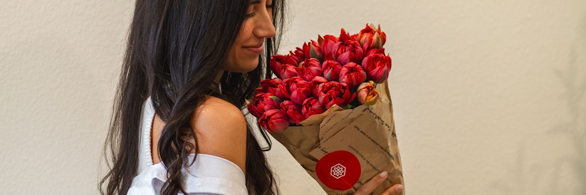 A woman lovingly holds a bouquet of vibrant red tulips wrapped in elegant paper.