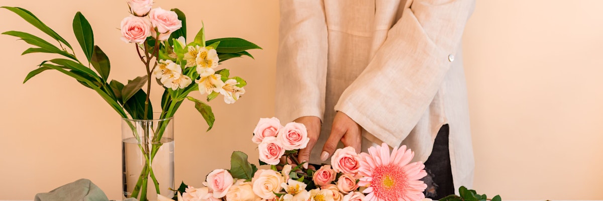 A person arranging a beautiful floral display featuring soft pink roses and vibrant gerbera daisies.