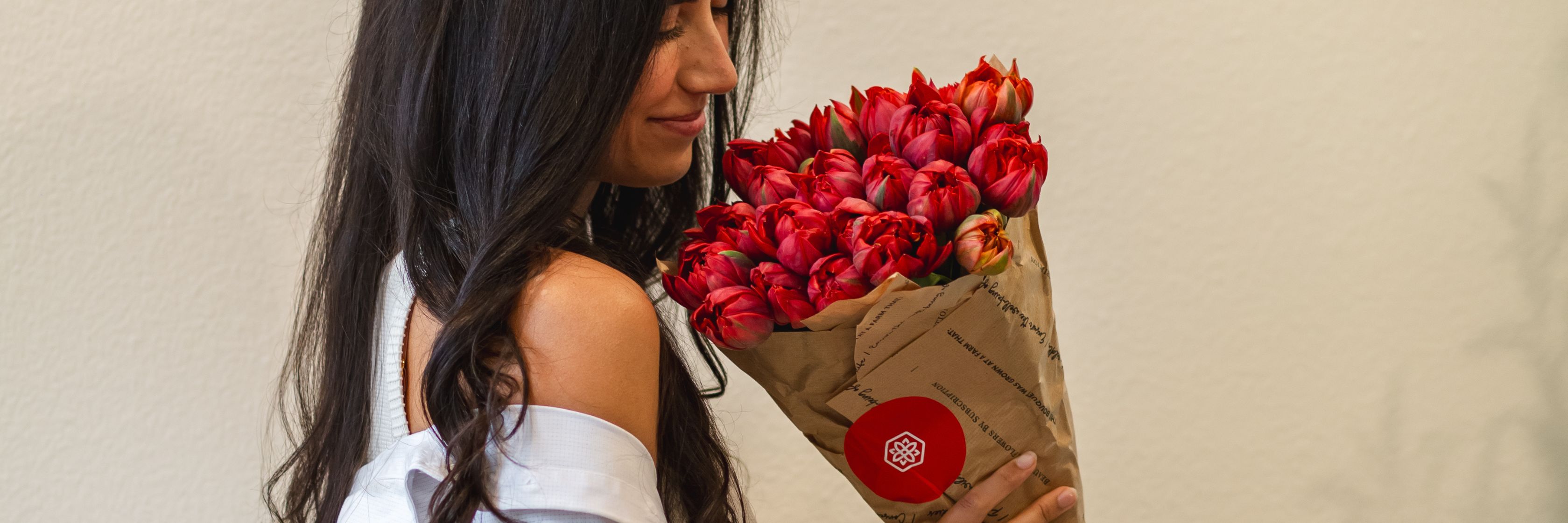 A woman admires a vibrant bouquet of red tulips in eco-friendly packaging, exuding elegance.
