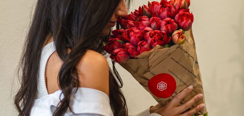 A woman enjoying a vibrant bouquet of red tulips wrapped in stylish paper, showcasing elegance.