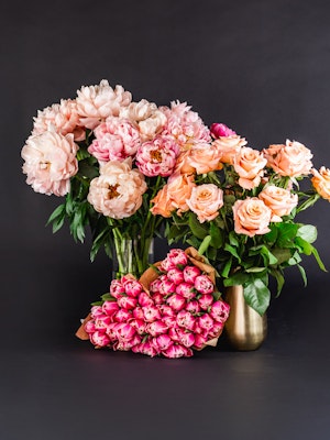 A vibrant arrangement of peonies and peach roses in elegant vases against a dark background.