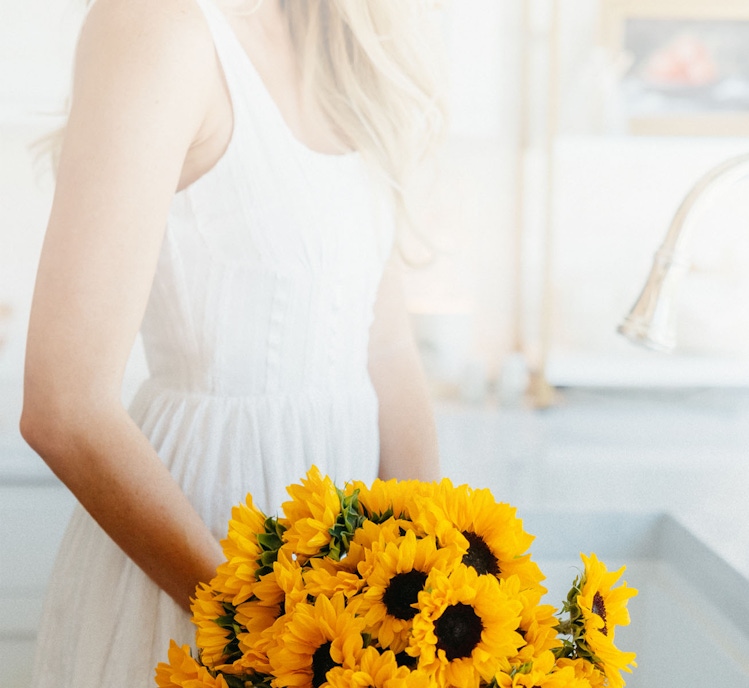 A woman in a white dress holds a vibrant bouquet of sunflowers, brightening the room.