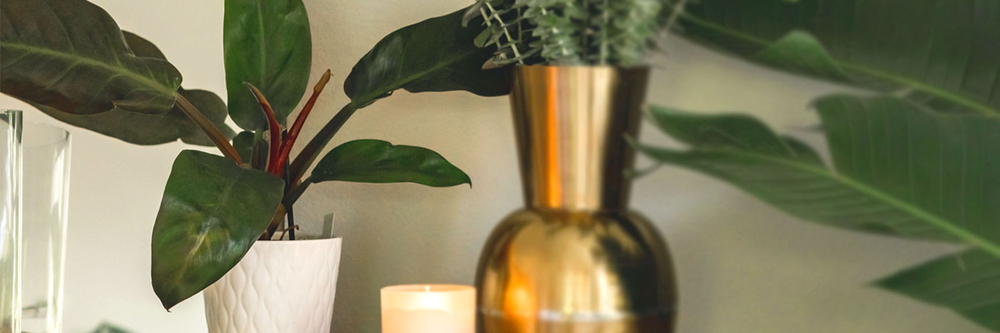 Stylish home decor featuring a gold vase with greenery, a white pot, and a lit candle for ambiance.
