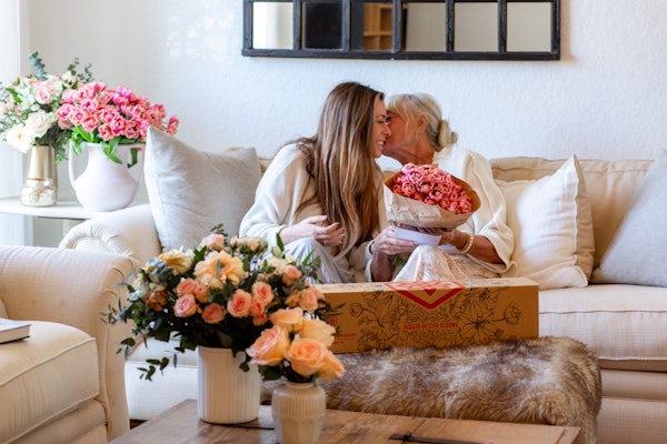 Two women share a joyful moment while admiring a beautiful bouquet of pink roses.