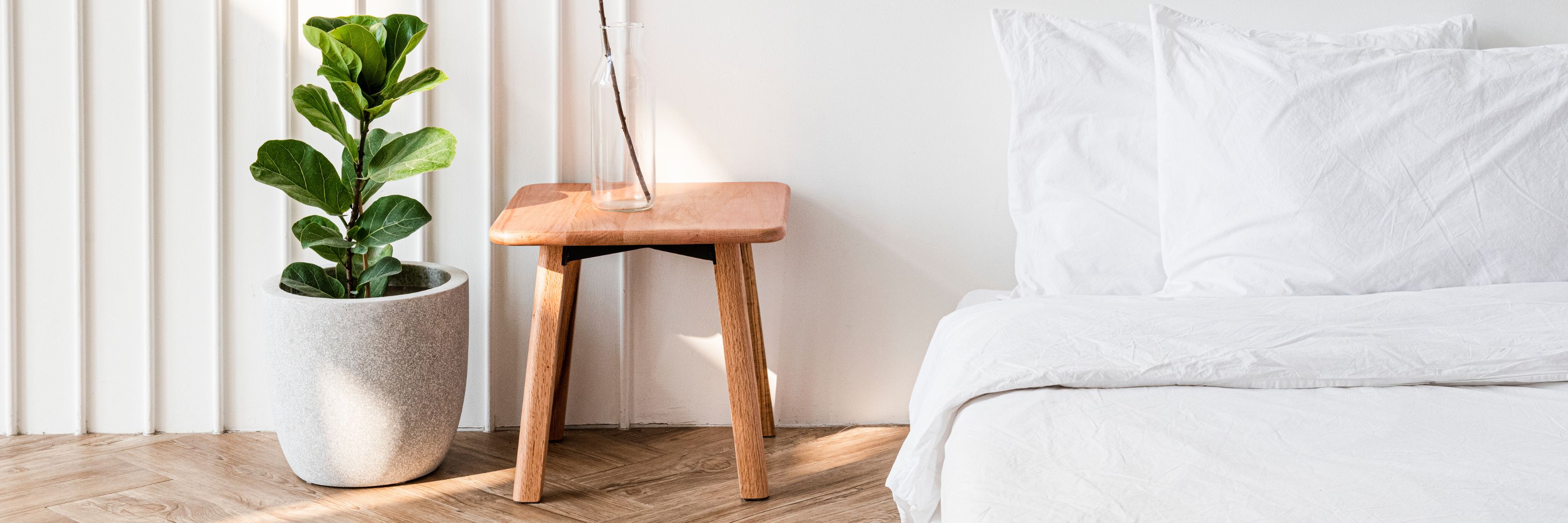 Minimalist bedroom setup featuring a cozy bed, sleek wooden side table, and a decorative plant.