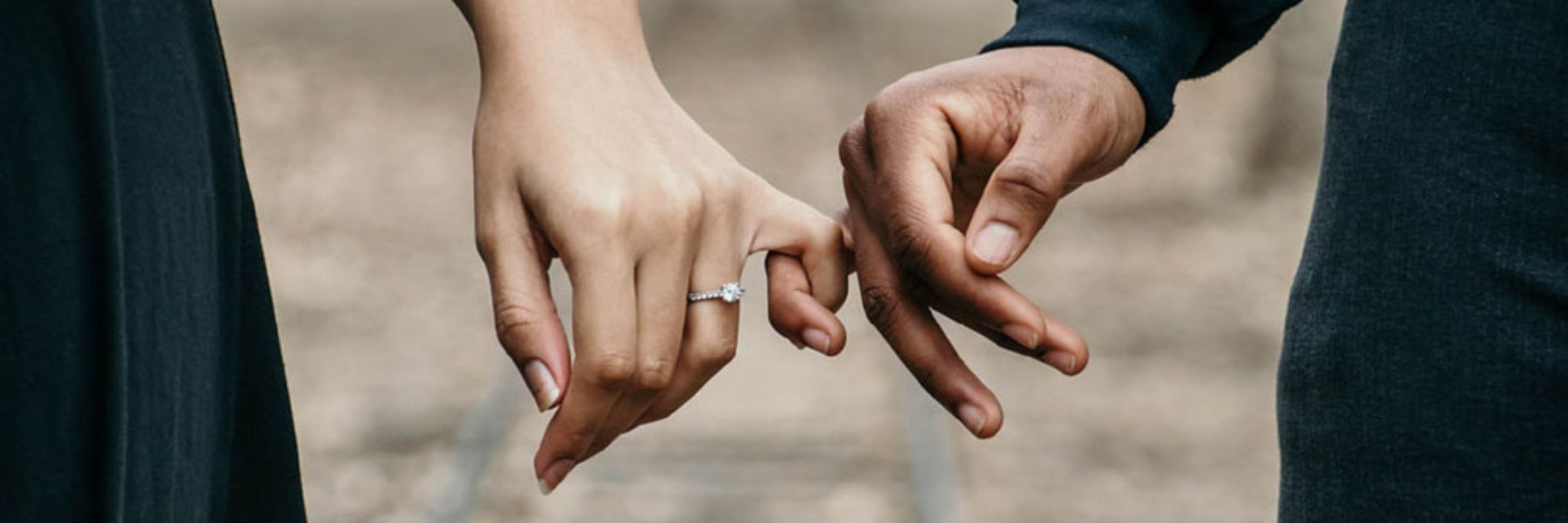 A couple holding hands, showcasing a beautiful engagement ring, symbolizing love and commitment.