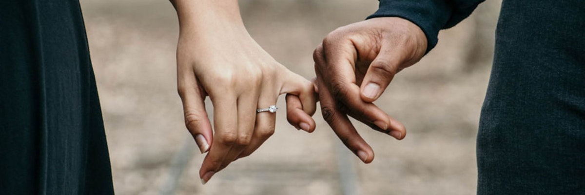 A couple holding hands, showcasing a beautiful engagement ring, symbolizing love and commitment.
