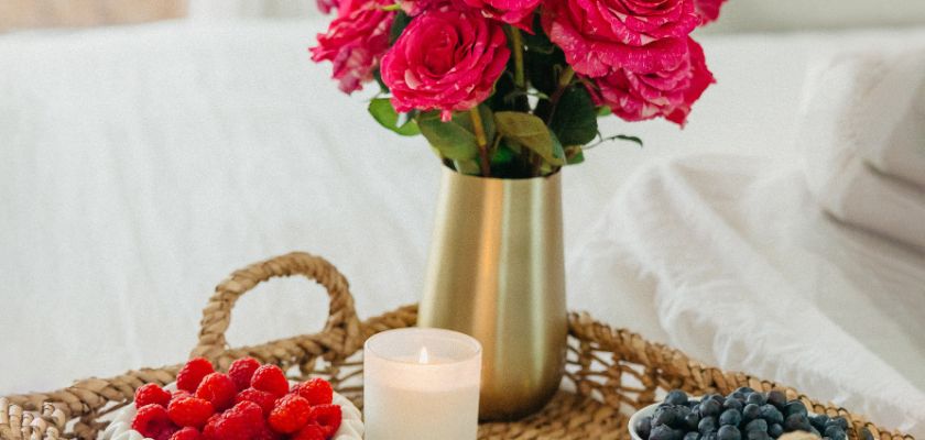 A charming arrangement of pink roses in a vase, paired with fresh berries and a candle.