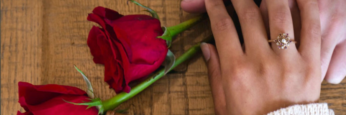 A romantic scene featuring two red roses beside a hand wearing an elegant ring, symbolizing love.