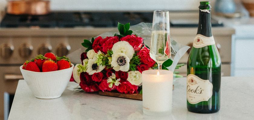 Elegant floral arrangement of red roses and white anemones with champagne and strawberries.