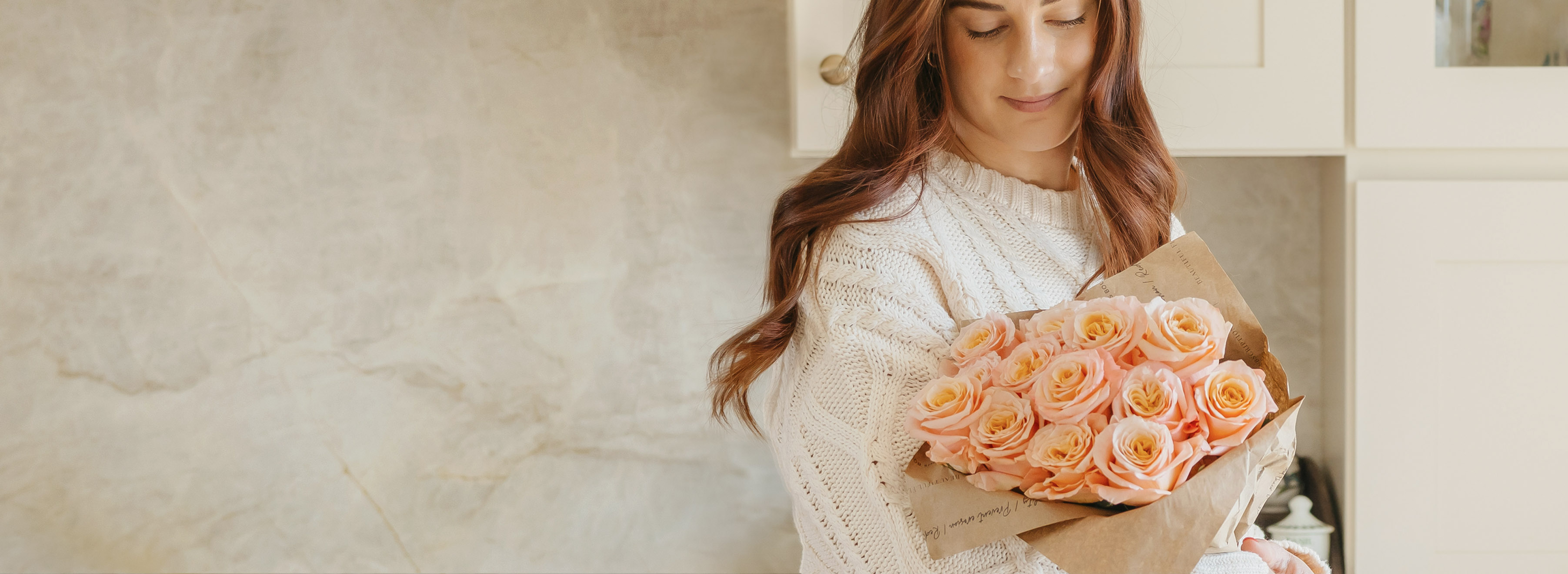 A woman in a cozy sweater holds a beautiful bouquet of soft pink roses, radiating warmth and charm.