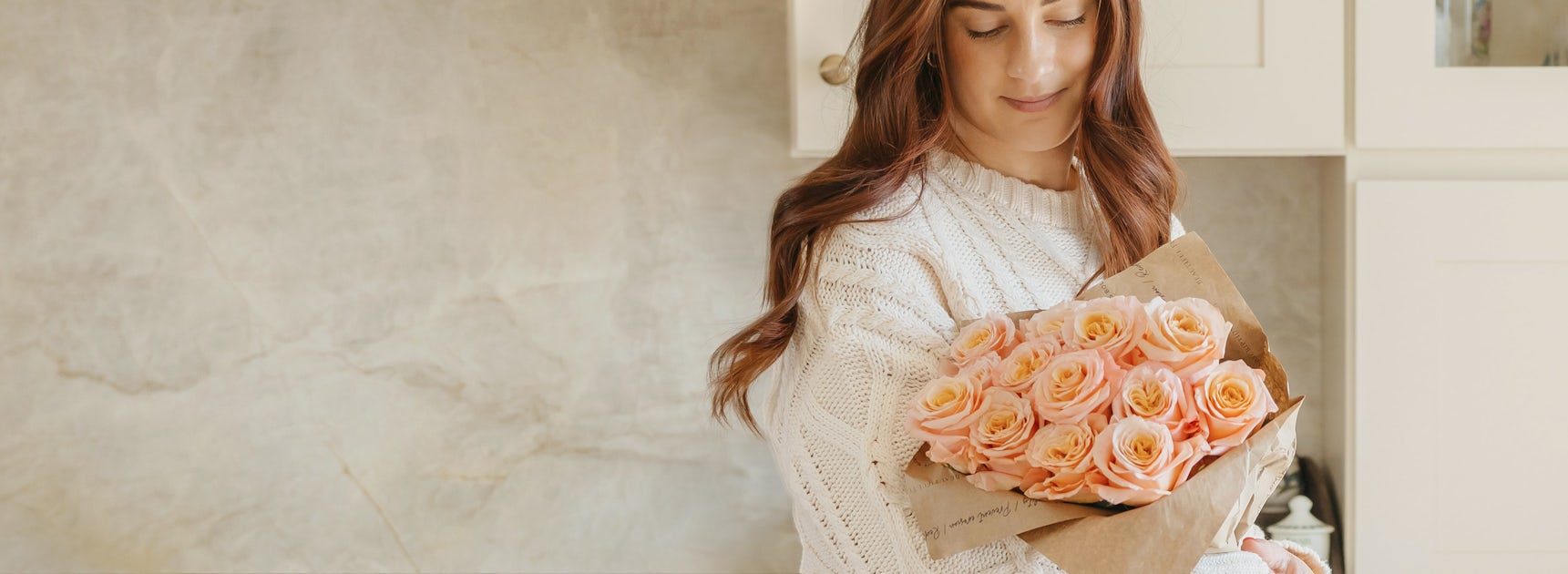 A woman in a cozy sweater holds a beautiful bouquet of soft pink roses, radiating warmth and charm.