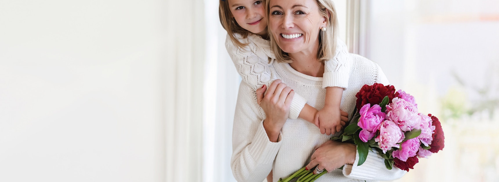 A joyful woman holding a colorful bouquet, smiling with her daughter embracing her from behind.