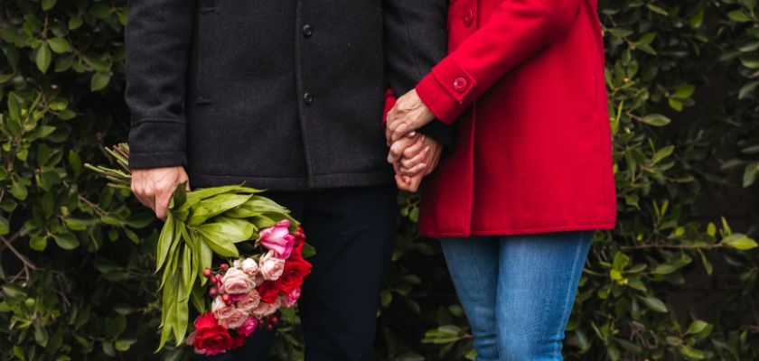 A couple holding hands and a beautiful bouquet of flowers, surrounded by lush green foliage.