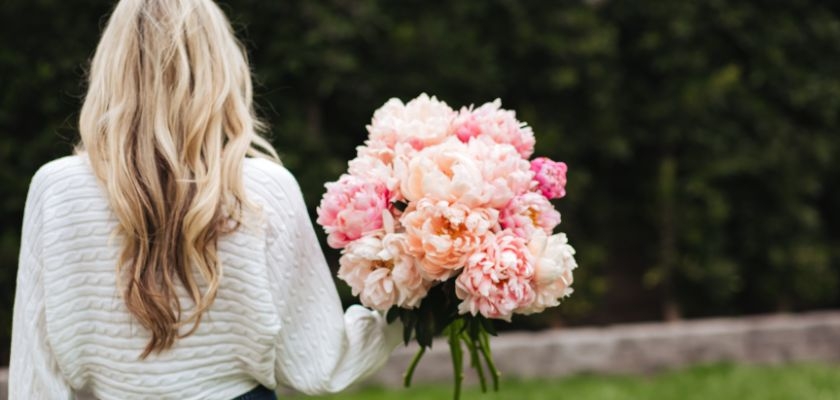 A woman holding a lush bouquet of blush and pink peonies, perfect for spring celebrations.