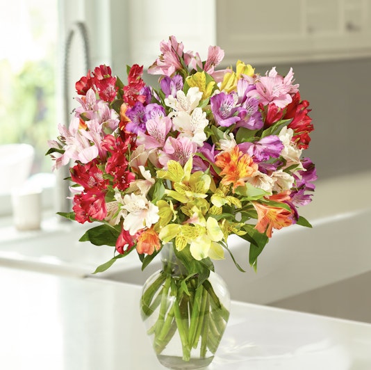 A vibrant bouquet of mixed alstroemeria flowers in a clear glass vase, brightening a kitchen.