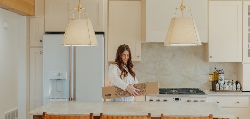Woman unboxing a floral delivery in a modern kitchen with light cabinetry and pendant lighting.