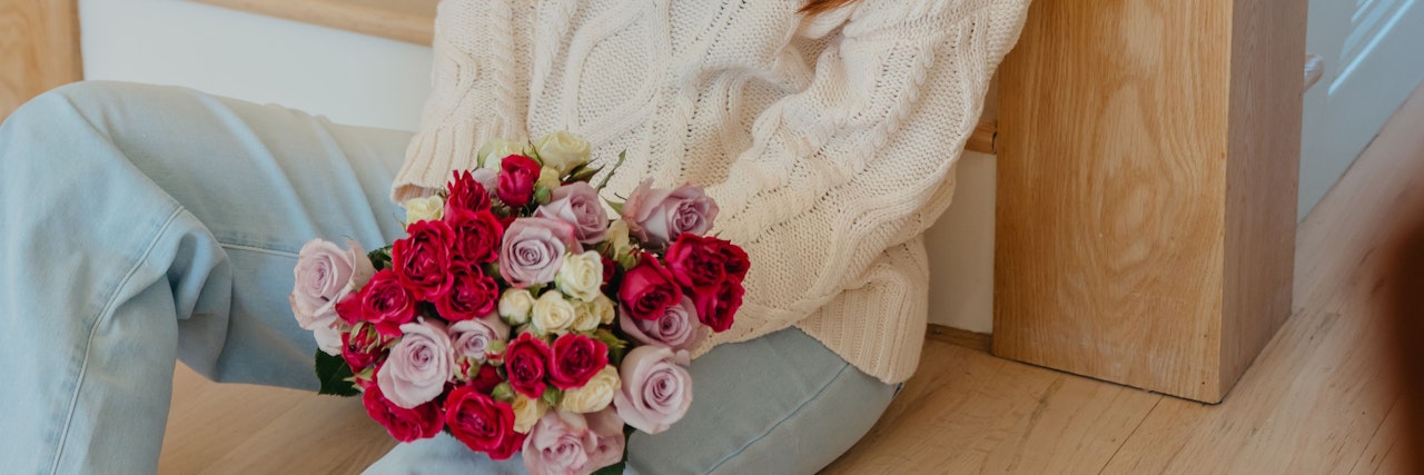 A woman in a cozy sweater sitting on the floor, holding a vibrant bouquet of roses.