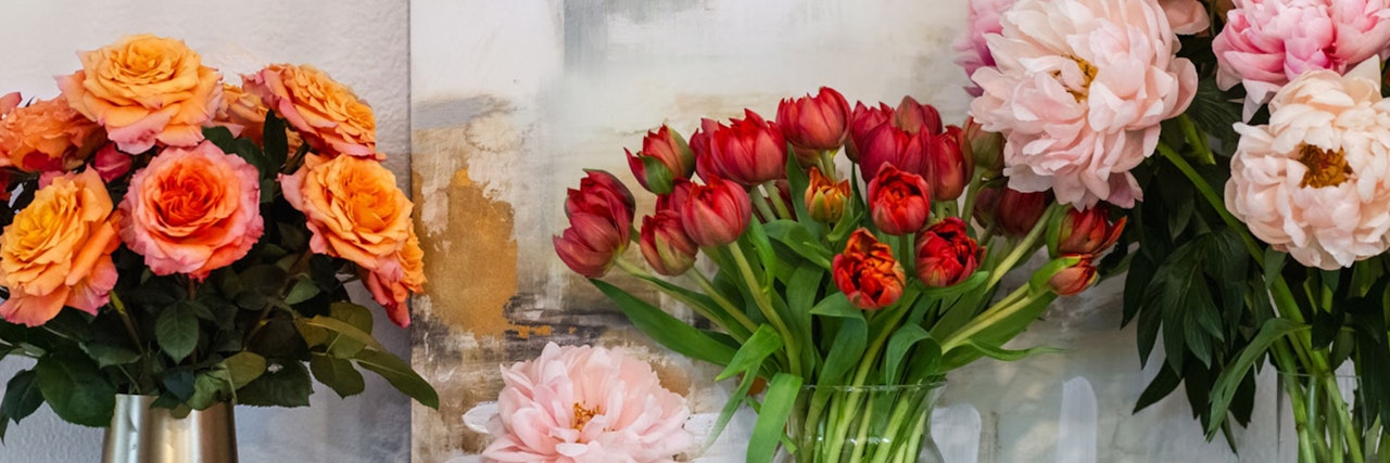 Vibrant floral arrangement featuring orange roses, red tulips, and pink peonies in elegant vases.