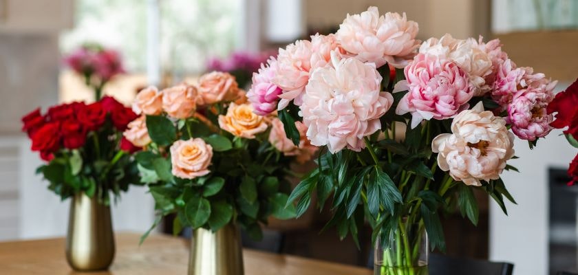 Lush floral arrangement featuring pink peonies and vibrant roses in elegant vases.