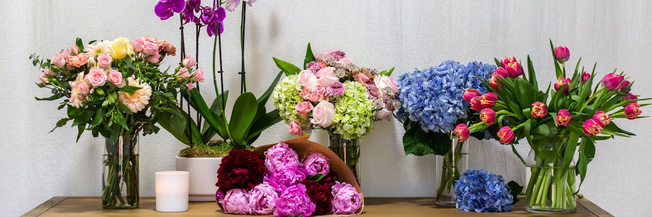 A vibrant flower display featuring pink roses, purple orchids, and colorful tulips in elegant vases.