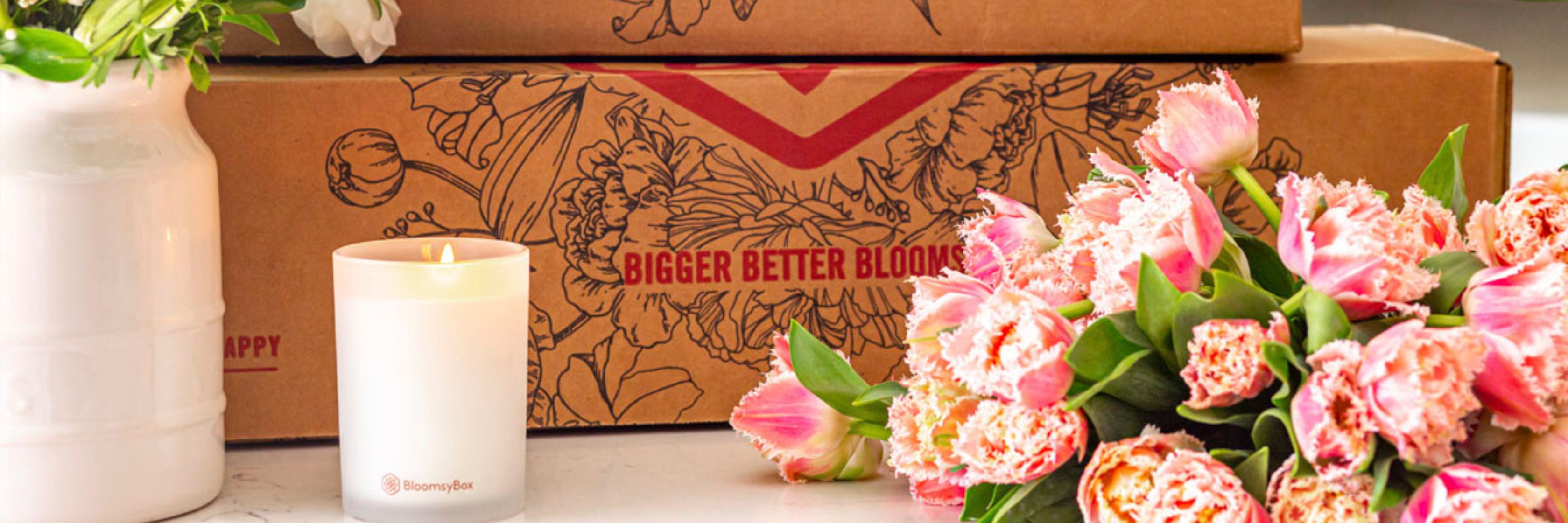 A beautiful arrangement of pink tulips alongside a lit candle next to a floral subscription box.