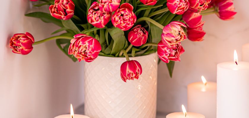 Vibrant pink tulips in a white vase surrounded by softly glowing candles, creating a warm ambiance.
