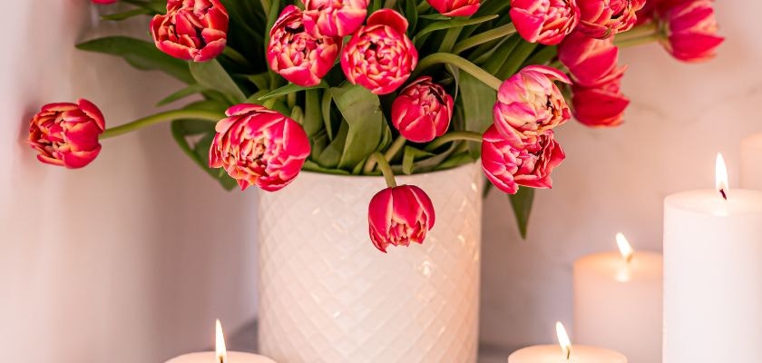 Vibrant pink tulips in a white vase surrounded by softly glowing candles, creating a warm ambiance.