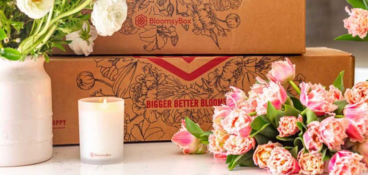 Charming arrangement of pink tulips beside a candle and BloomsBox delivery boxes on a marble table.