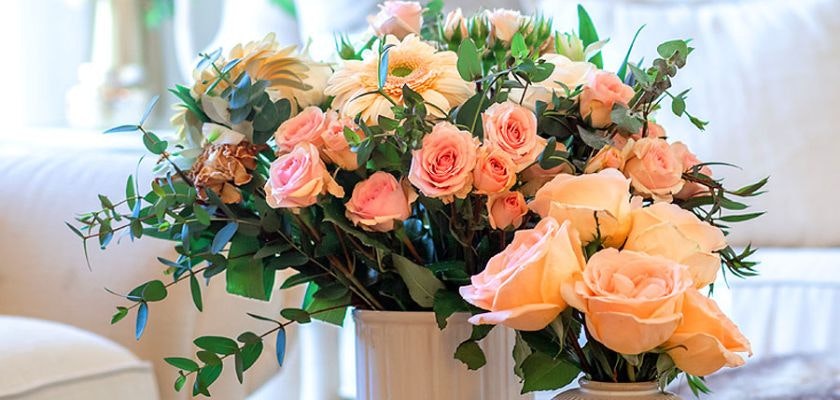Delicate floral arrangement featuring pink and peach roses among lush greenery in elegant vases.