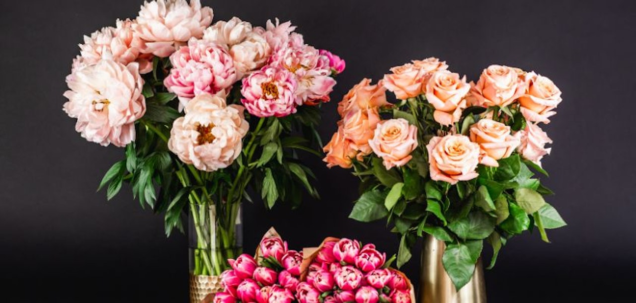 Elegant floral display featuring pink peonies and peach roses in stylish vases.