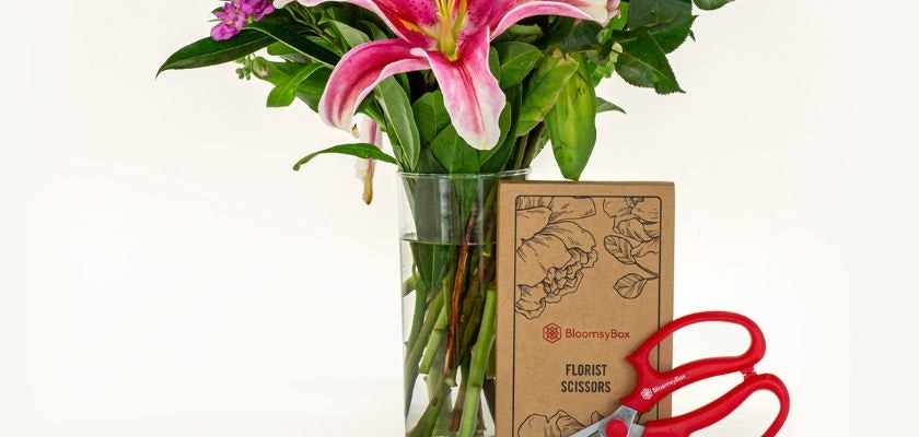 Elegant floral arrangement with lilies, greenery, and florist scissors in a stylish vase.