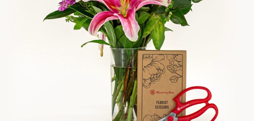 Elegant floral arrangement with lilies, greenery, and florist scissors in a stylish vase.