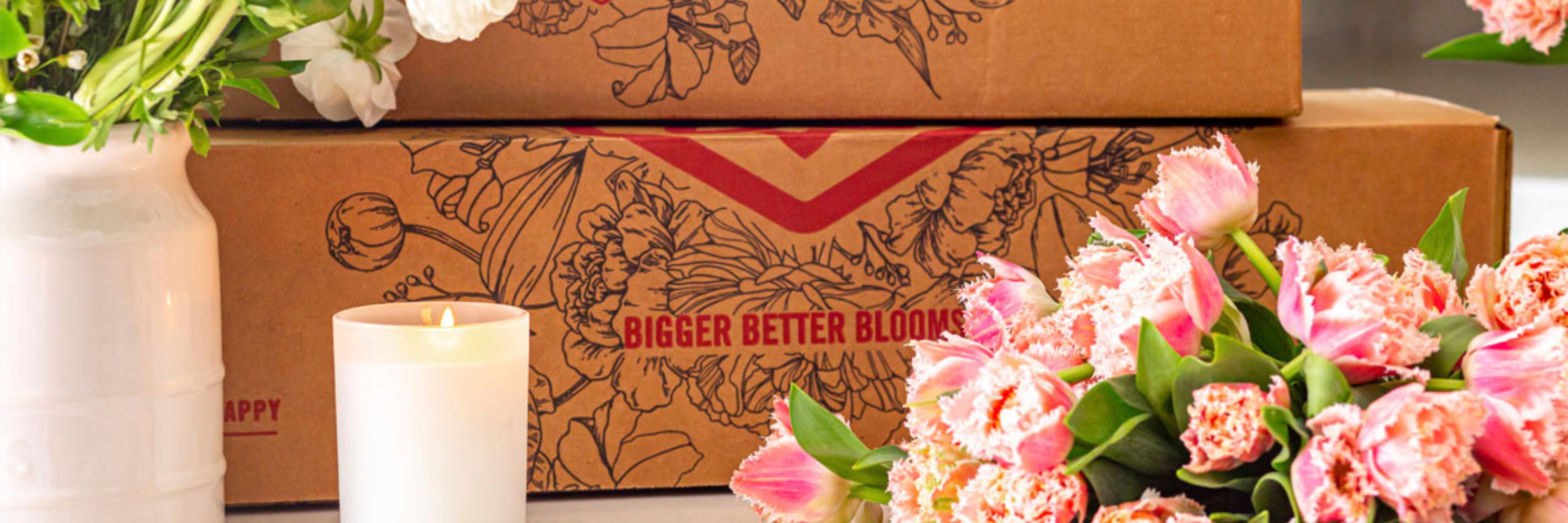 Delicate pink tulips arranged alongside floral gift boxes and a lit candle.