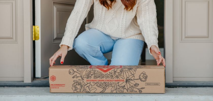 A woman in a cozy sweater receiving a sustainable floral delivery box at her doorstep.
